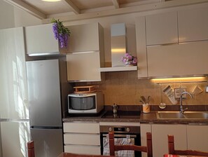 A kitchen with a refrigerator, microwave, oven, and a wooden chair.