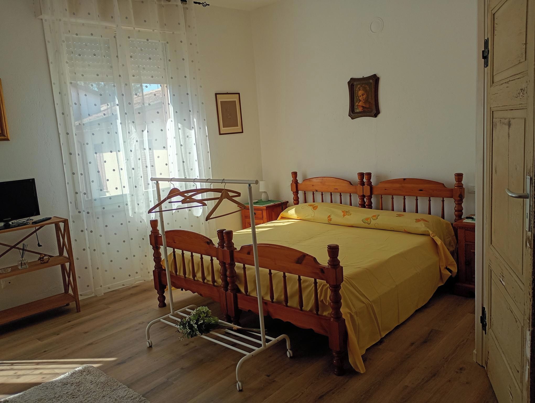 Ein Schlafzimmer mit einem hölzernen Bett, einem Nachttisch, einem Hängekorbsessel und einem Fenster mit Vorhängen.