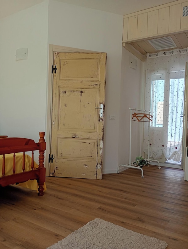 Une pièce avec une porte en bois, un banc rouge, un radiateur blanc et une fenêtre avec des rideaux.