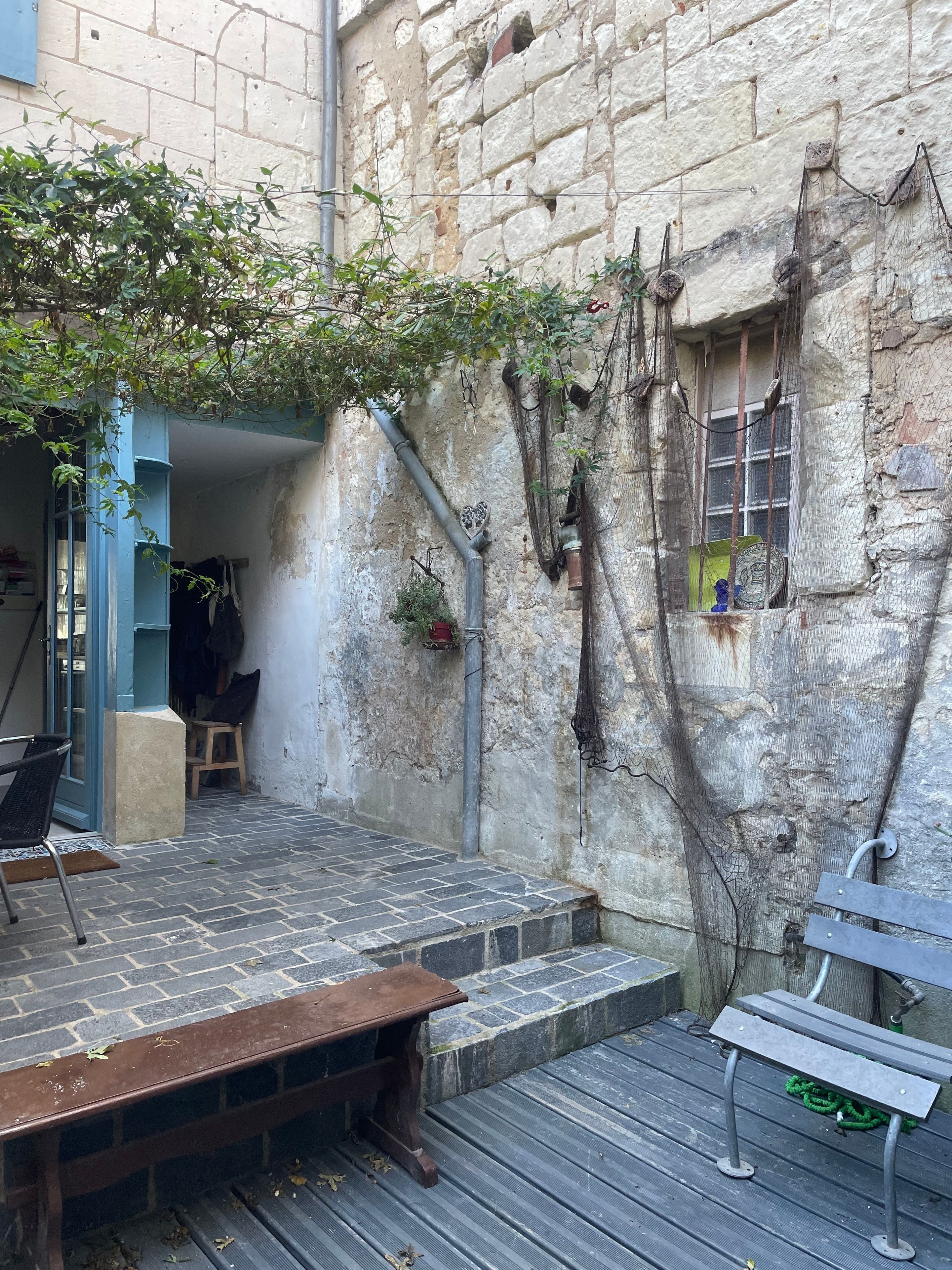 A courtyard with a wooden bench, a metal bench, and a stone wall with a window.