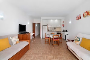 Ein Wohnzimmer mit einer Couch, einem Fernseher und einem Essbereich mit Tisch und Stühlen.