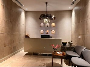 A modern reception area with a desk, chairs, a decorative light fixture, and wall-mounted displays. - Super Luxury Condo in Bomonti Elisiyum Art (Istanbul)