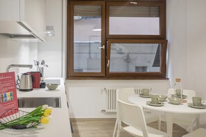 A modern kitchen with a window, white cabinets, and a dining area with a table set for two. - XXV Aprile By Wonderful Italy - Menta (Genoa)