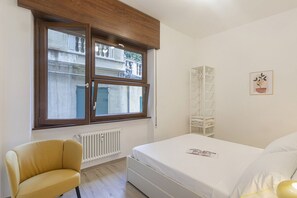 A bedroom with a bed, a chair, a radiator, a window, and a wall-mounted shelf. - XXV Aprile By Wonderful Italy - Menta (Genoa)