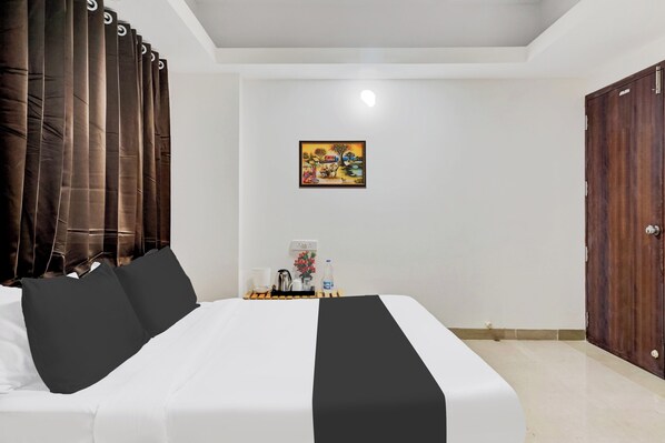 A hotel room with a bed, a painting, a nightstand with a bottle, and a wooden door.