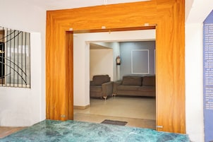 A room with a wooden door leading to a living area with two sofas and a fire extinguisher on the wall.