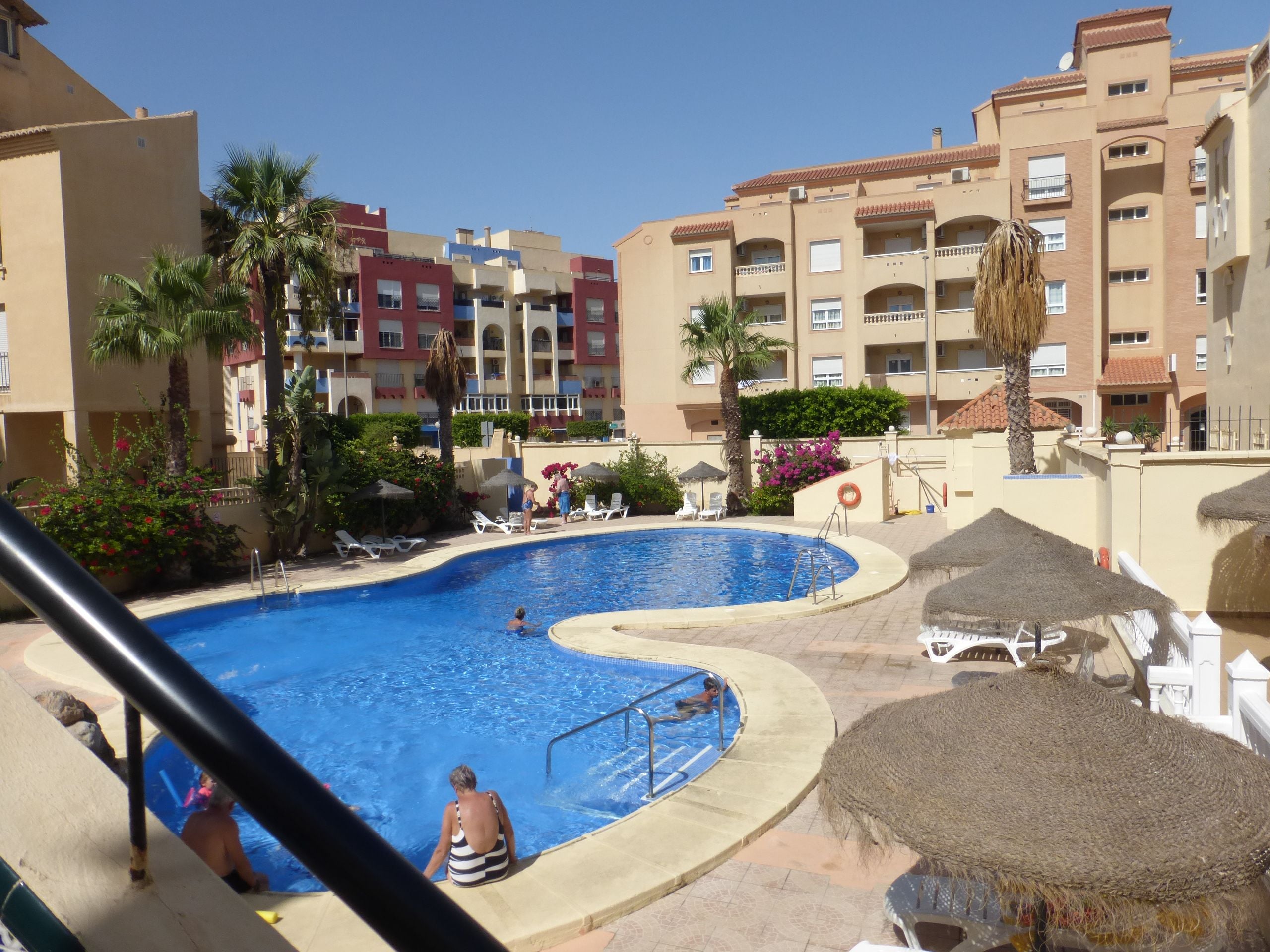 A swimming pool surrounded by lounge chairs and umbrellas, with a building in the background.