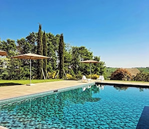 A swimming pool with clear water, surrounded by a wooden deck, and two white lounge chairs with umbrellas. - "Villa Vernaschi – Heart of Le Marche" (Marche)