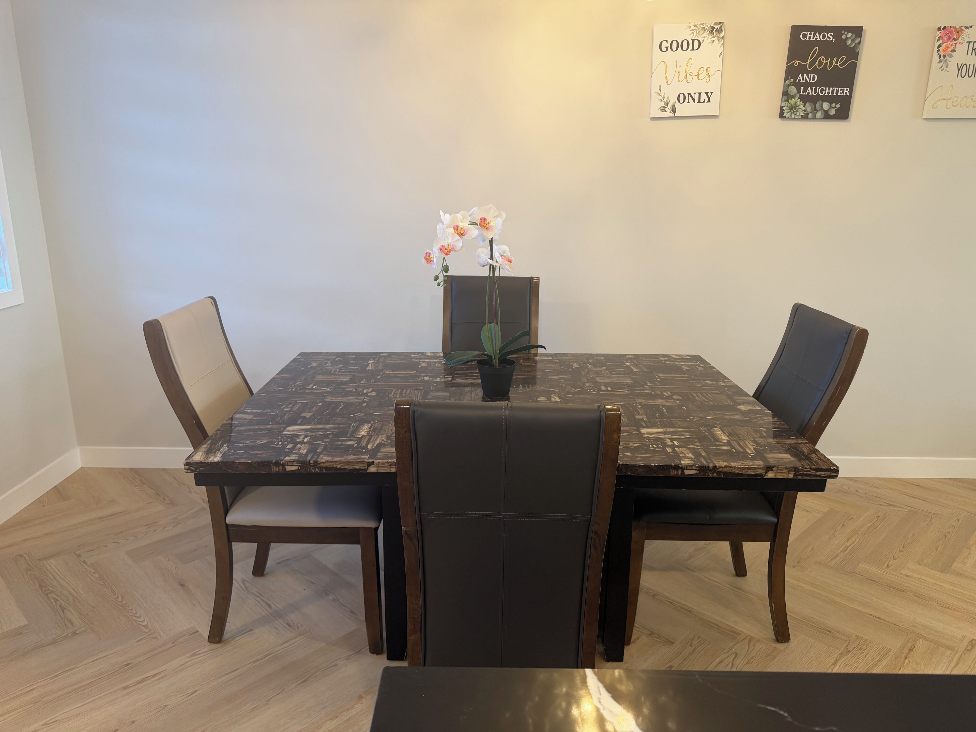 A dining table with chairs, a potted plant, and decorative wall art.