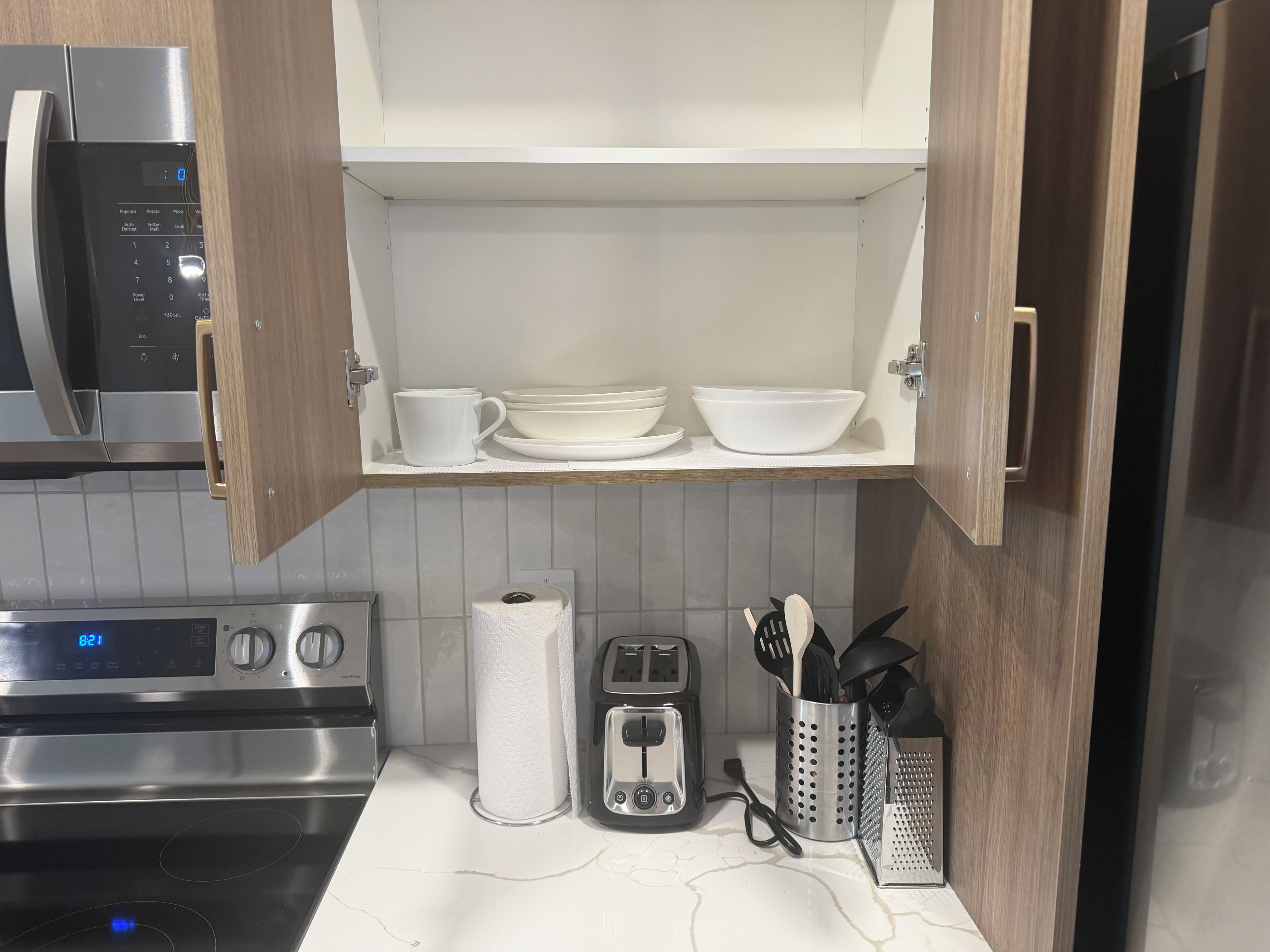 A kitchen with a microwave, toaster, and a shelf with dishes.