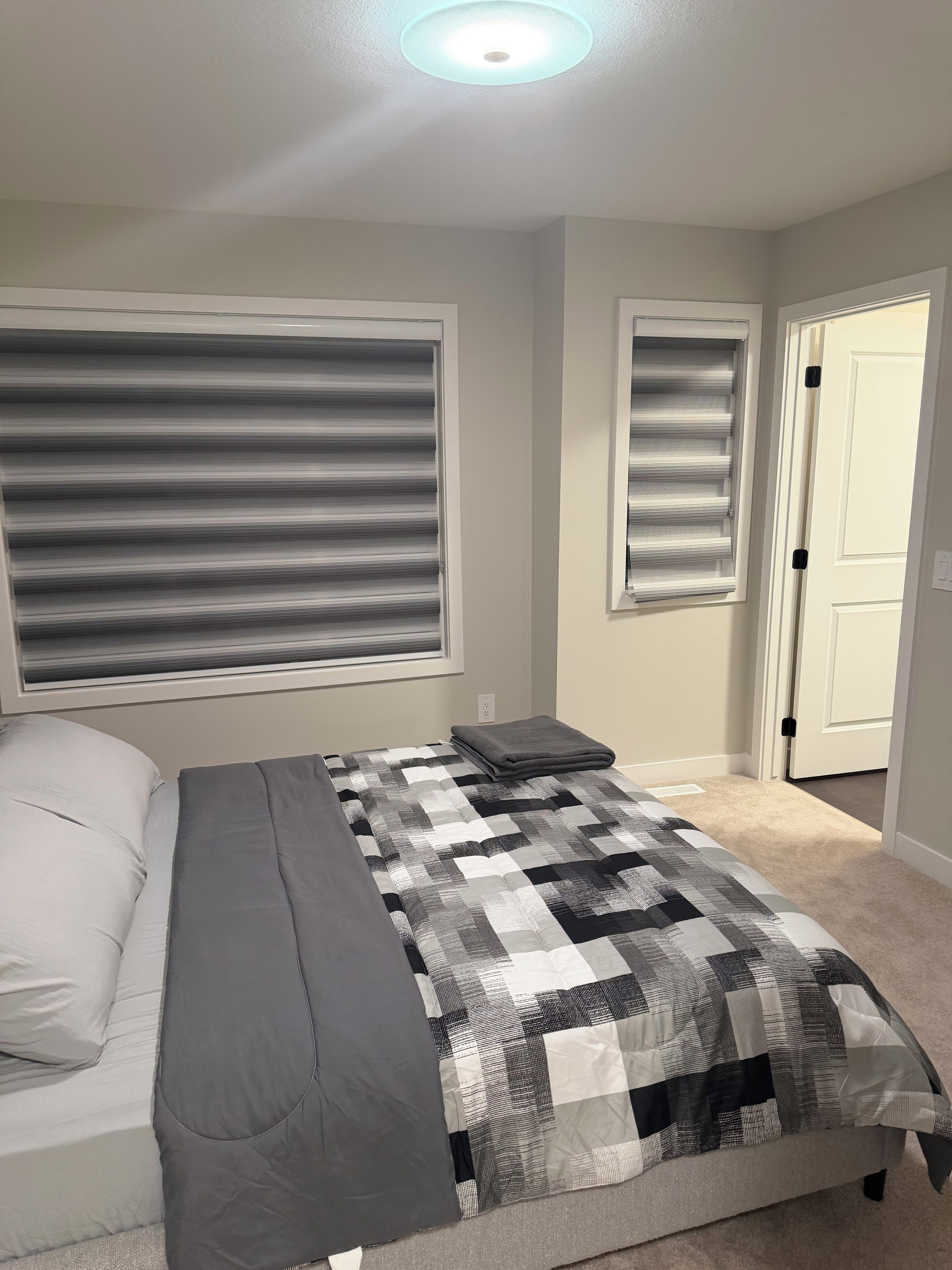 A bedroom with a bed, a window with blinds, a door, and a carpeted floor.