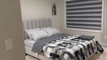 A bedroom with a bed, a window with blinds, a ceiling light, and a wall-mounted picture.