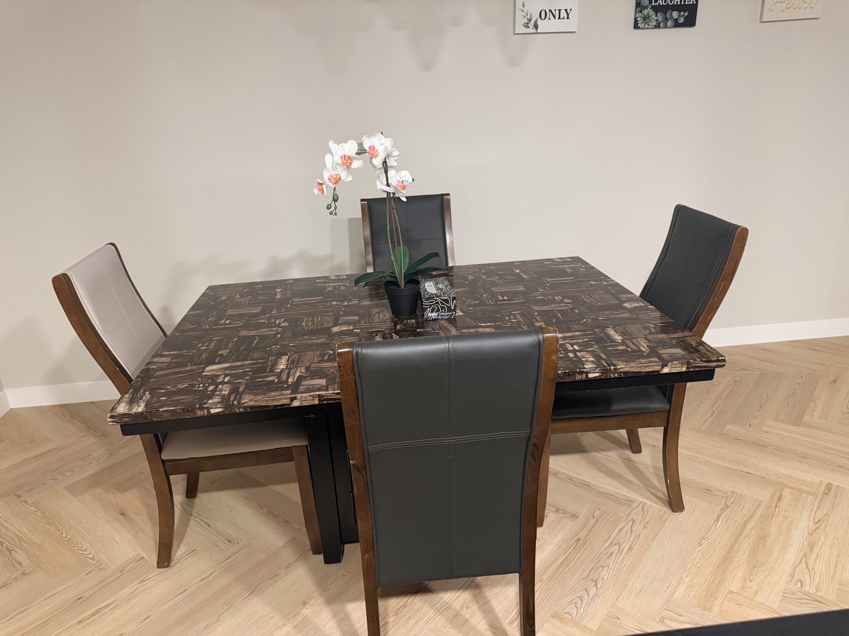 A dining table with a dark patterned tablecloth, surrounded by four chairs with wooden frames and dark upholstery.