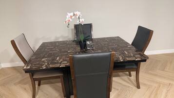 A dining table with a dark patterned tablecloth, surrounded by four chairs with wooden frames and dark upholstery.