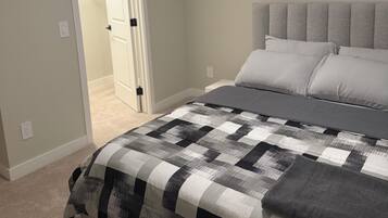 A bedroom with a bed, a door leading to another room, and a wall-mounted artwork.