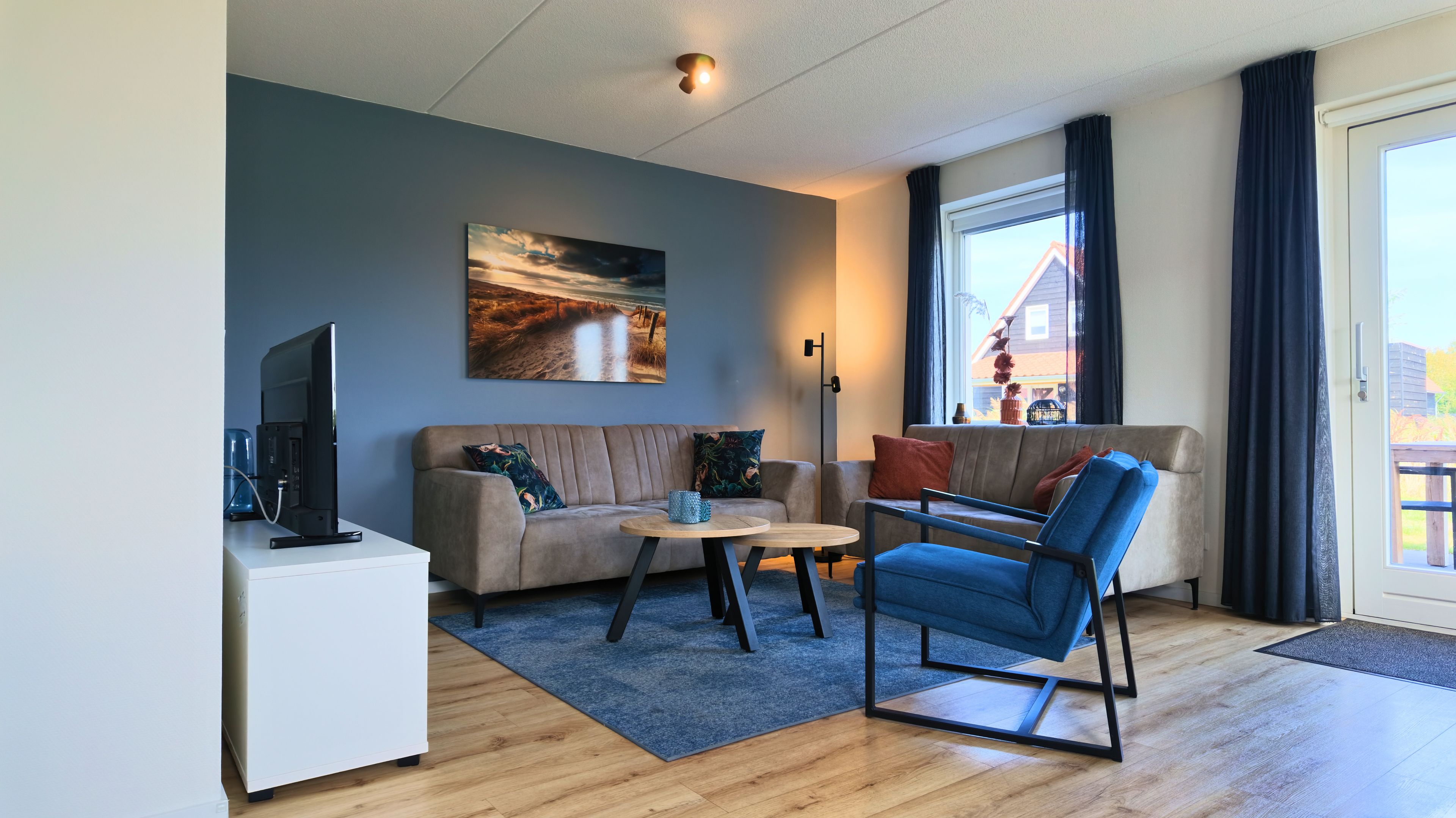 Ett modernt vardagsrum med en soffa, ett soffbord, en tv och ett stort fönster med gardiner.
