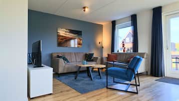 Ett modernt vardagsrum med en soffa, ett soffbord, en tv och ett stort fönster med gardiner.