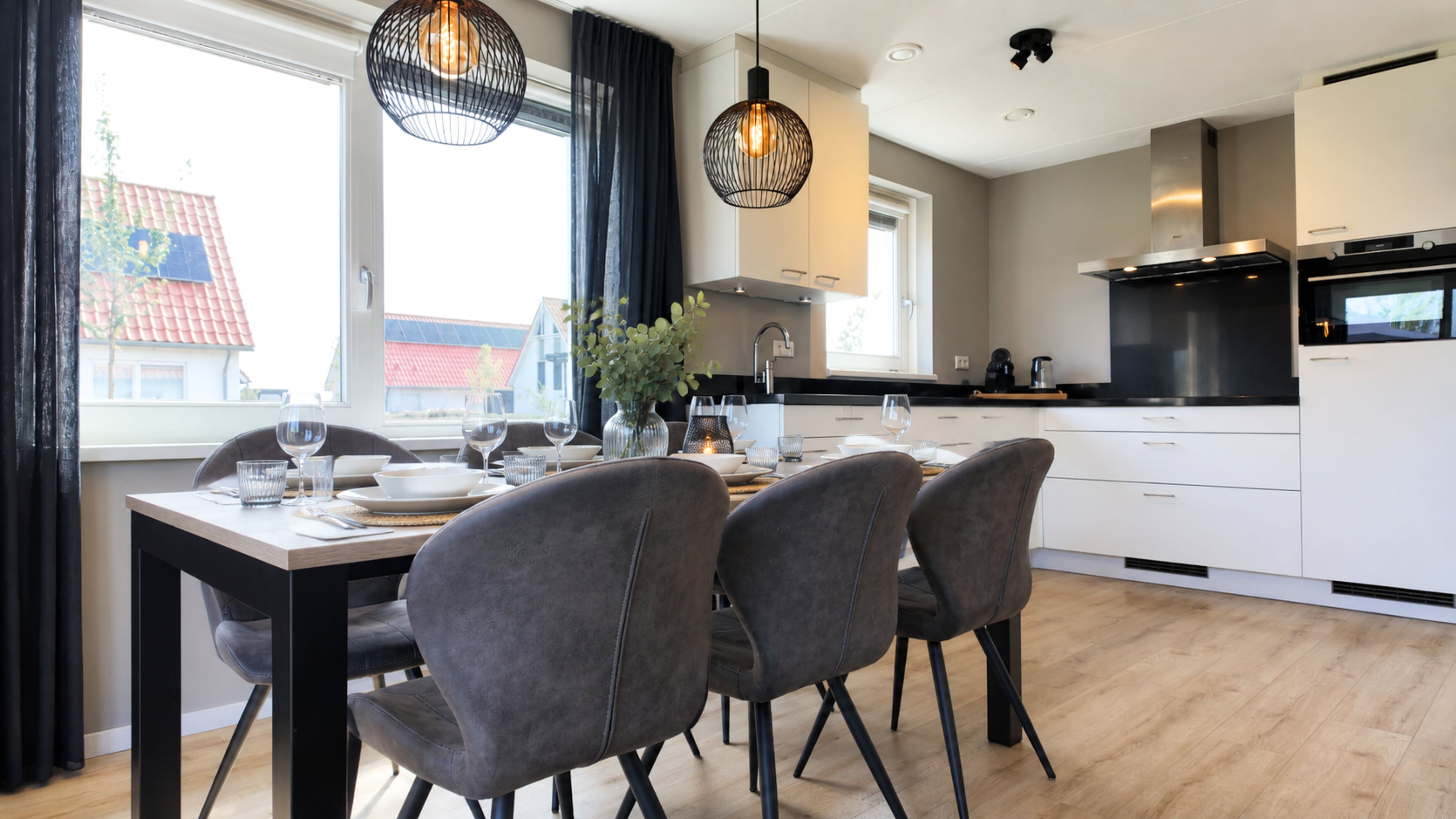 Una cucina moderna con mobili bianchi, un tavolo da pranzo con sedie e lampadari a sospensione.