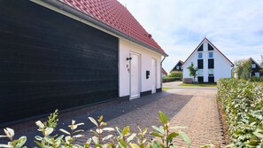 En bostadsgata med en svartvit byggnad, en asfalterad uppfart och en häck.