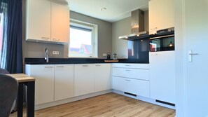 Ett modernt kök med vita skåp, en svart bänkskiva och ett fönster med utsikt över en byggnad med rött tak.