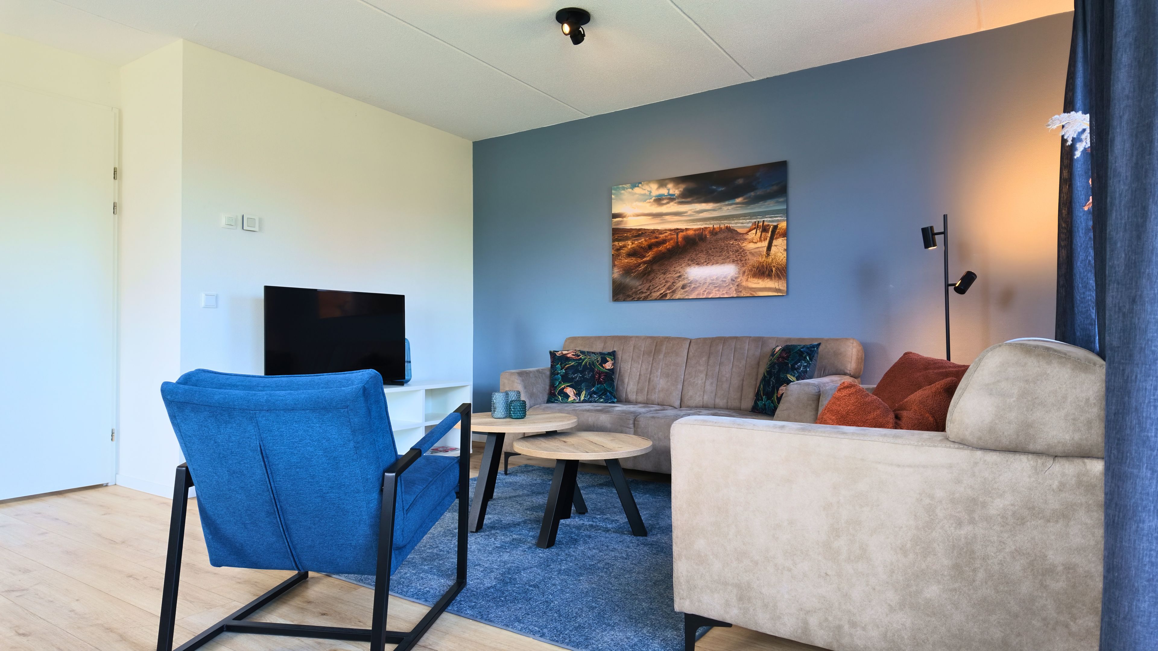 A living room with a sofa, a blue chair, a coffee table, and a flat-screen TV.