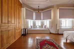 Ein Schlafzimmer mit einem Holzschrank, einem Bett mit weißer Bettwäsche, einem gemusterten Teppich und einem Erkerfenster mit Vorhängen.