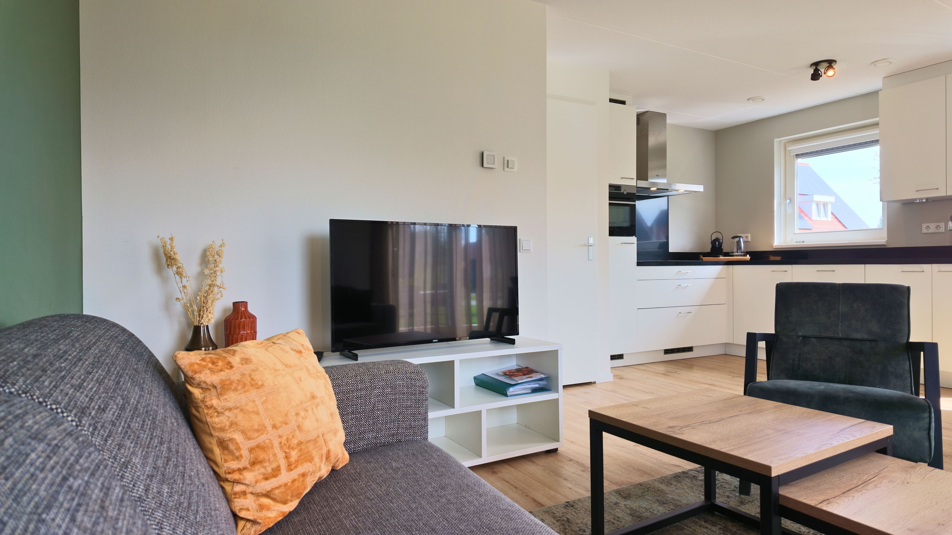 Ein modernes Wohnzimmer mit Fernseher, einer Couch, einem Couchtisch und einer Küche im Hintergrund.