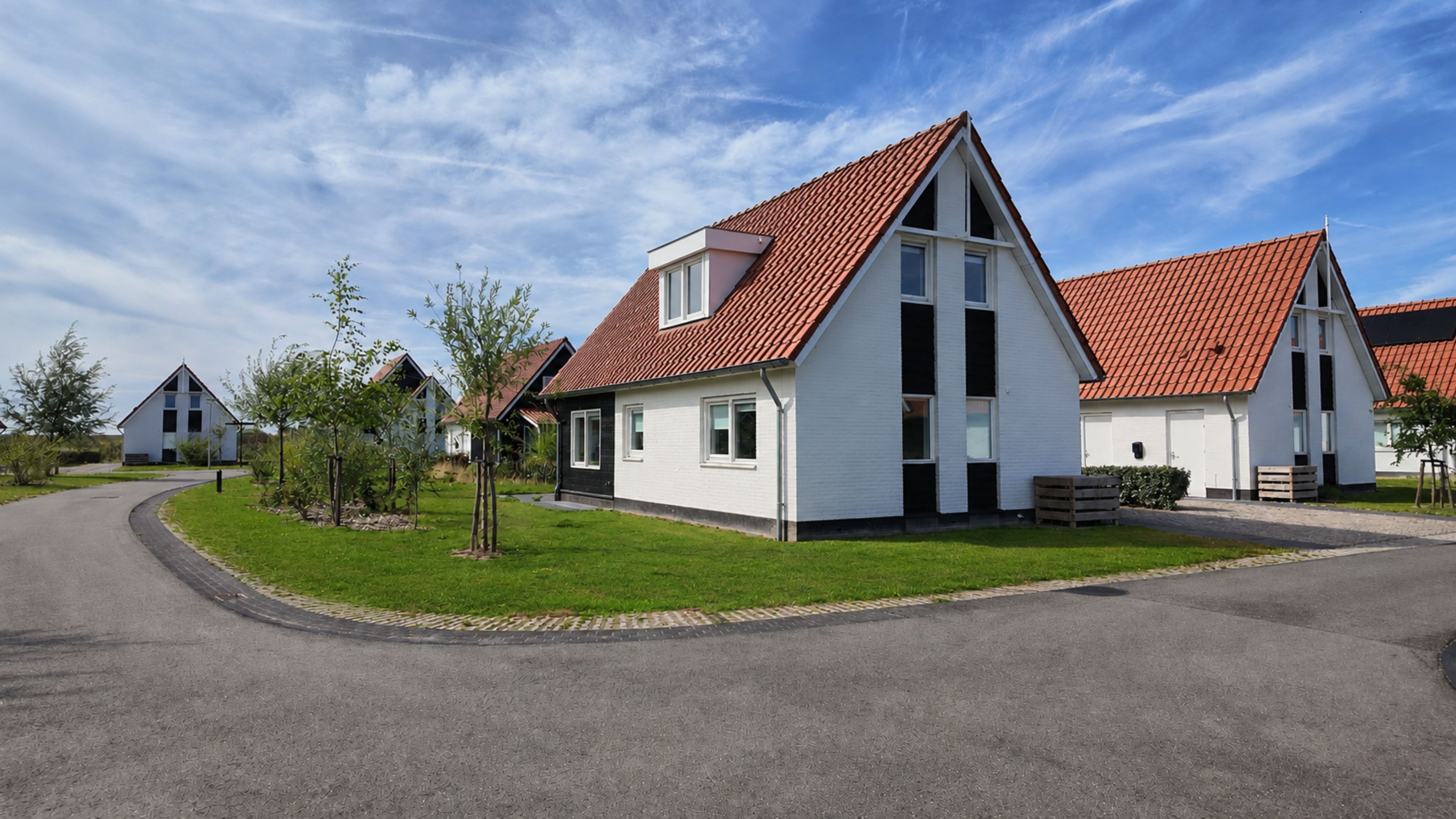 Een rij moderne huizen met rode pannendaken, witte muren en een verzorgd gazon.