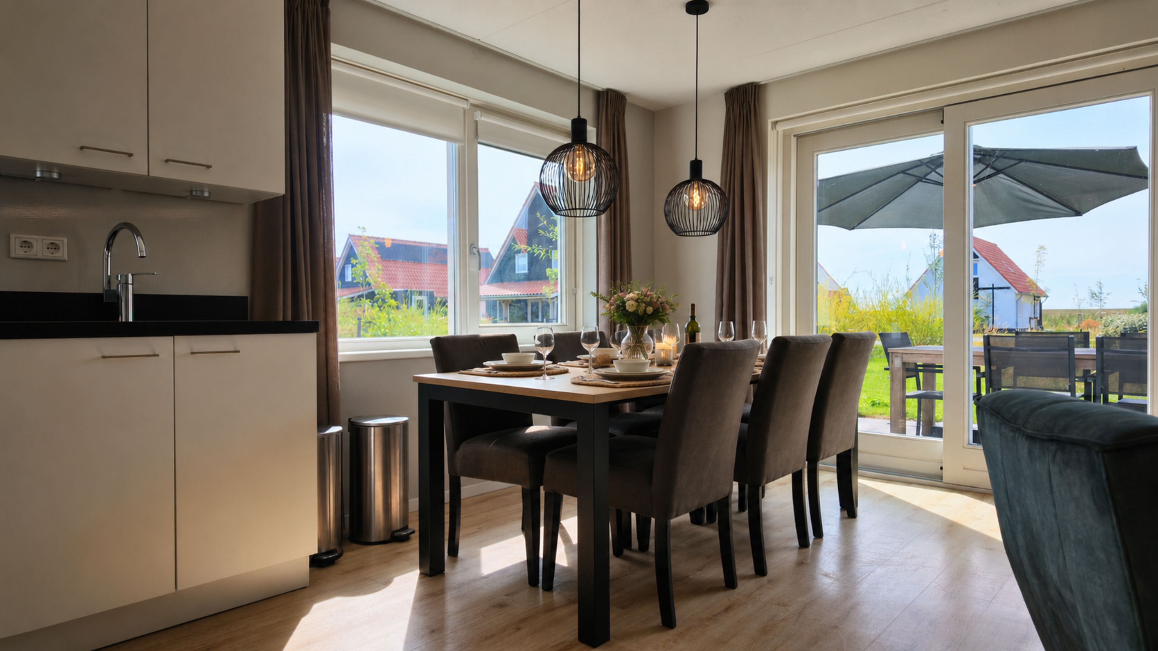 A modern kitchen with a dining area, large windows, and a view of the outside.