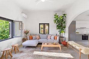A modern living room with a sofa, coffee table, and a large plant. - The Palms Seaside - Kolymvari (Kolymvari)