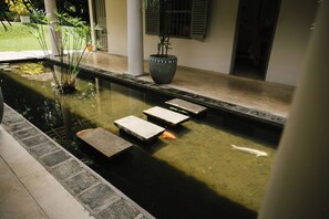 A koi pond with stepping stones, surrounded by a tiled walkway and potted plants. - Oba Samaga by TONIK (Unawatuna)
