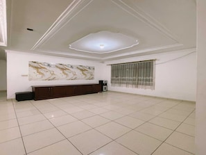 Una habitación amplia con piso de baldosas, un mueble de madera oscura, una obra de arte de mármol en la pared y una ventana con cortinas de encaje.