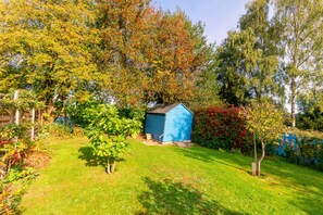 Un jardin bien entretenu, avec un abri bleu, différents arbres et une pelouse.