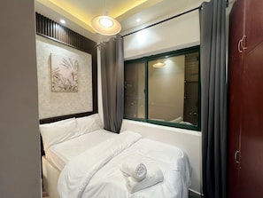 Een hotelkamer met een bed, een raam met gordijnen, een aan de muur hangend kunstwerk en een plafondlamp.