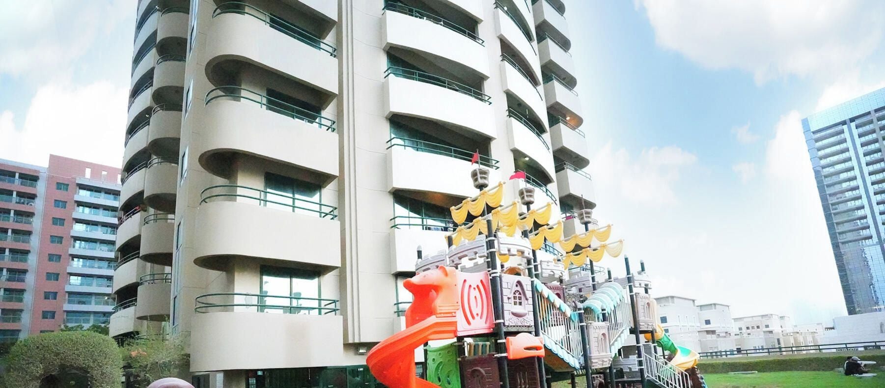 A multi-story building with balconies and a playground structure with slides and climbing elements.