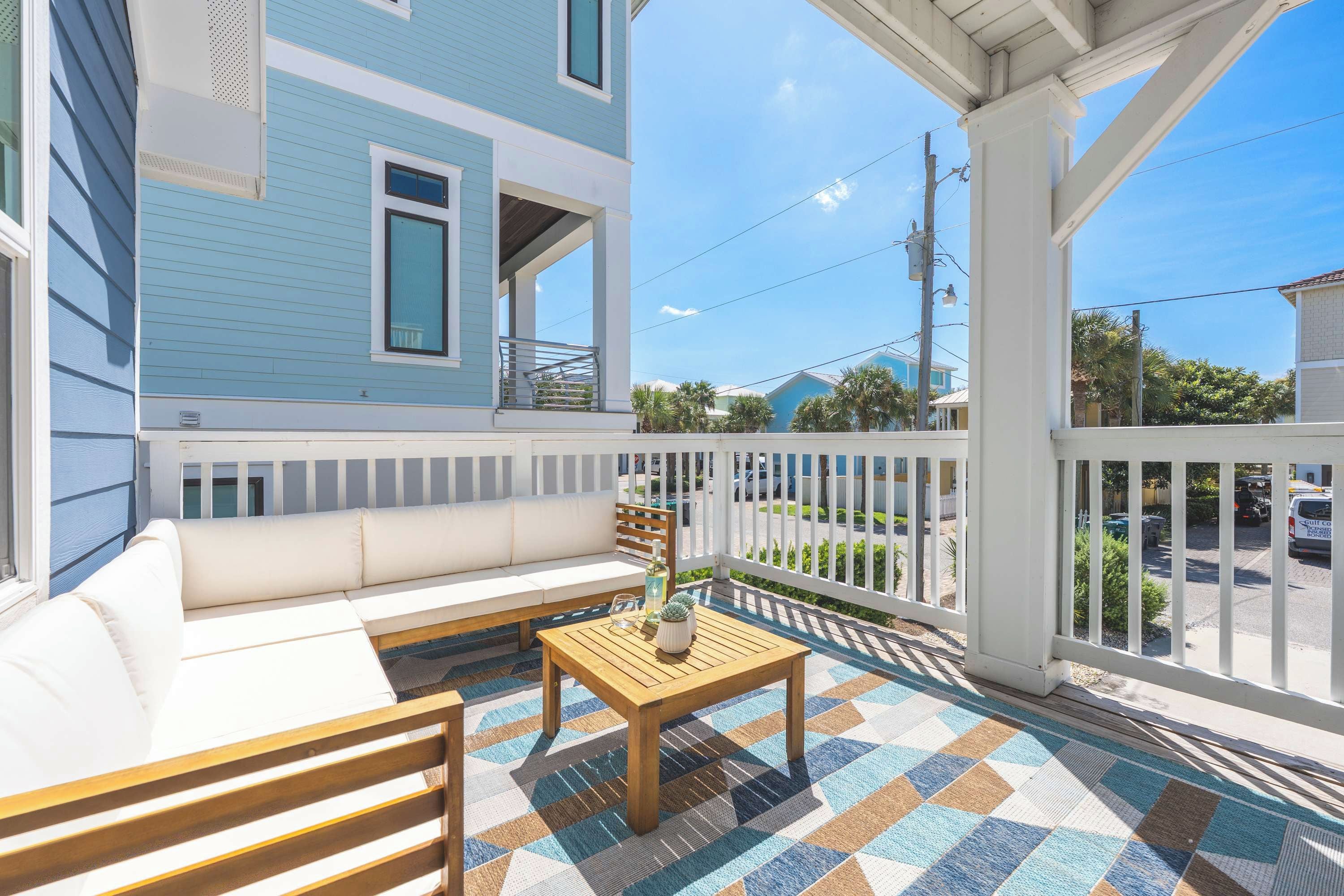 A covered porch with a sofa, a wooden table, and a patterned rug.