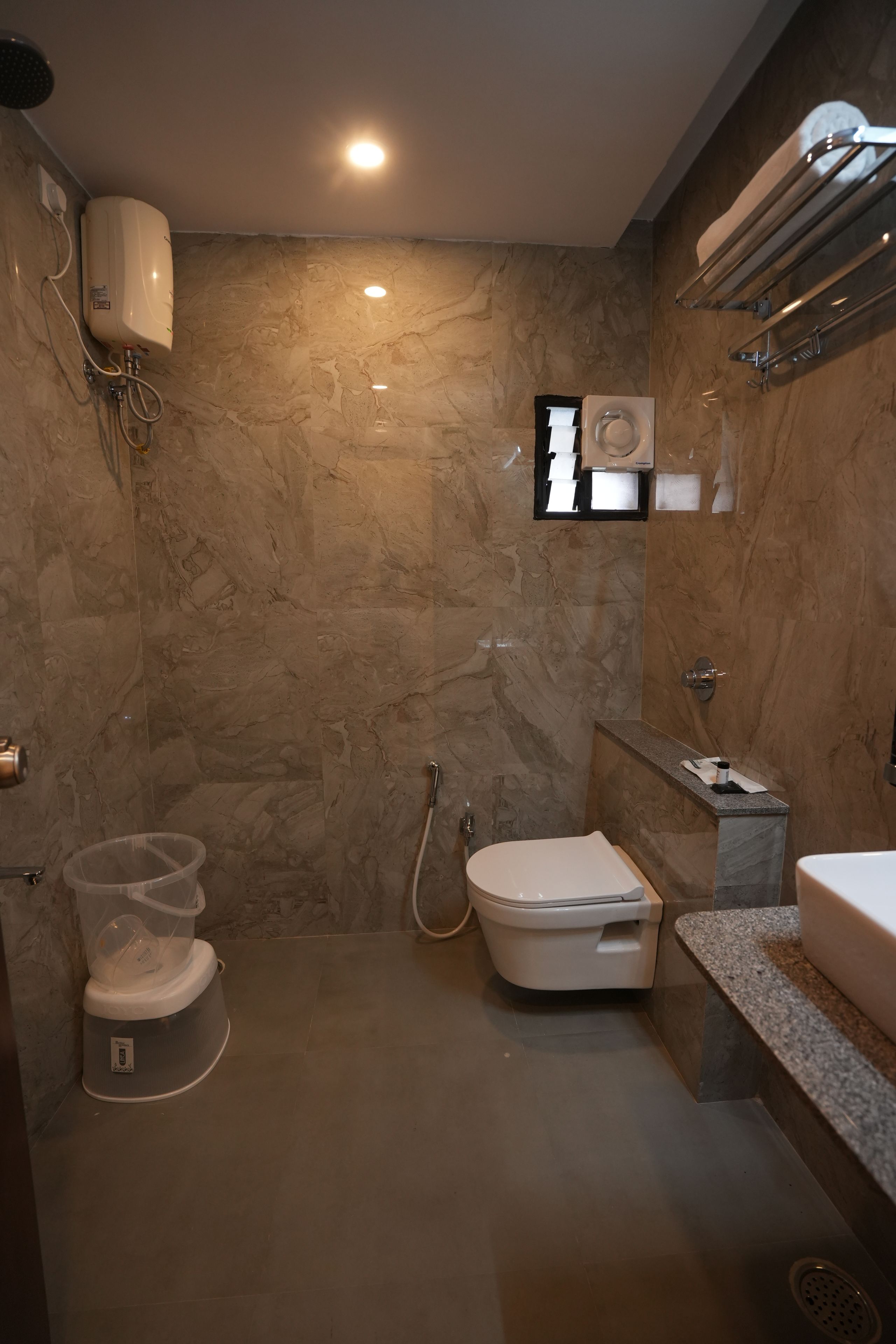 A modern bathroom with a marble wall, a toilet, a shower, and a sink.