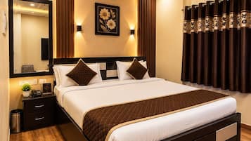 A hotel room with a bed, bedside table, nightstand, wall-mounted air conditioning unit, ceiling fan, and a large mirror.