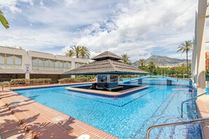 A swimming pool with a thatched-roof structure, surrounded by palm trees and a mountain in the background. - BENAL BEACH: Ocean View with Excellent Wi-Fi (Benalmádena Costa)