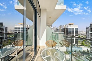 A modern balcony with glass railings, two wicker chairs, and a glass table. - Bloomfields Studio in Azizi Riviera 43 (Dubai)