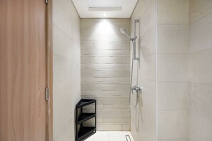 A small, narrow bathroom with a shower, a wooden door, and a black shelf unit. - Bloomfields Studio in Azizi Riviera 43 (Dubai)