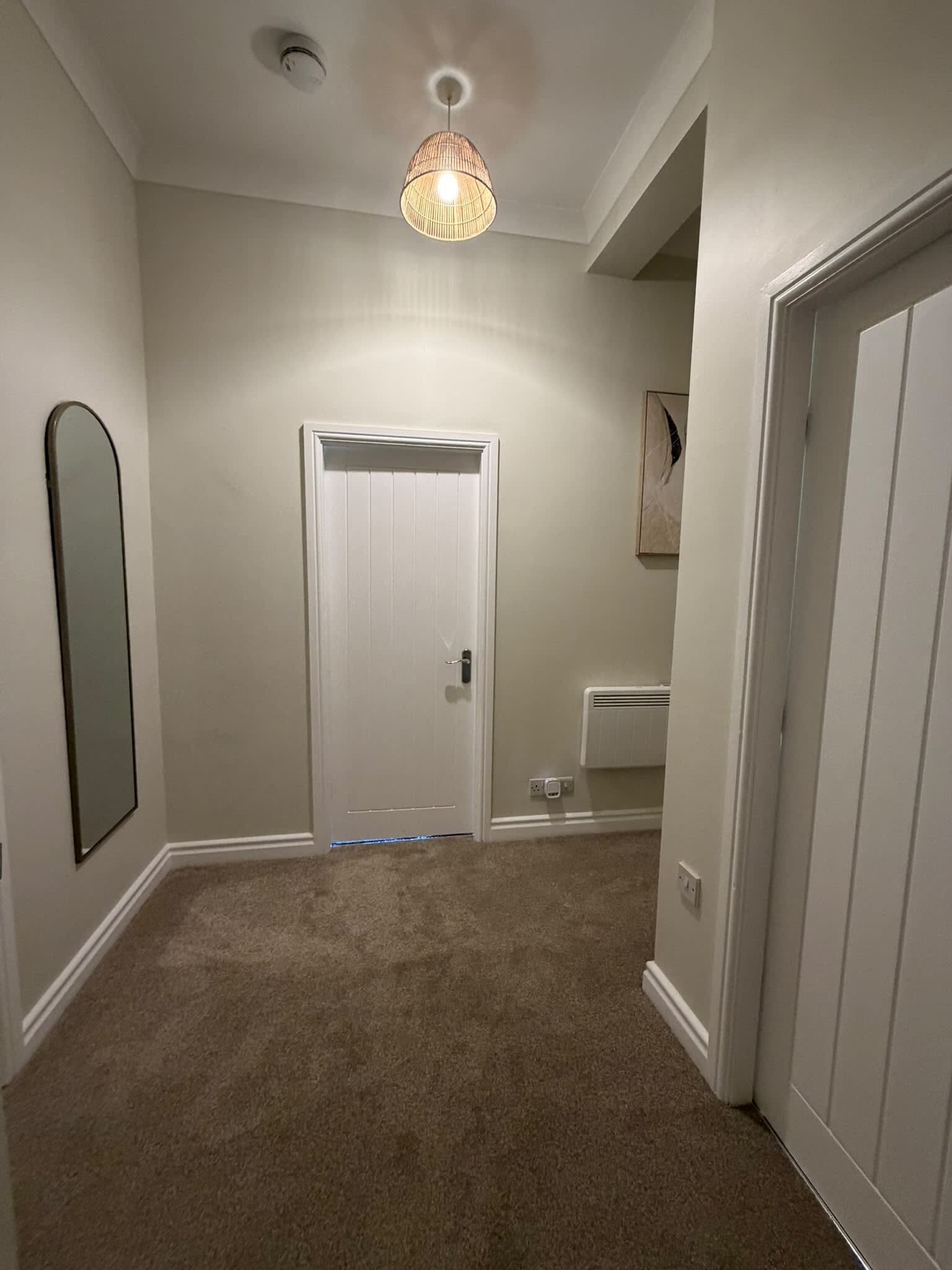 A hallway with a white door, a mirror on the left, and a light fixture on the ceiling.