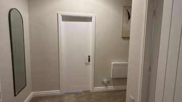A hallway with a white door, a mirror on the left, and a light fixture on the ceiling.