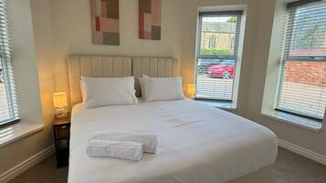 A bedroom with a large bed, two bedside lamps, and two windows with blinds.