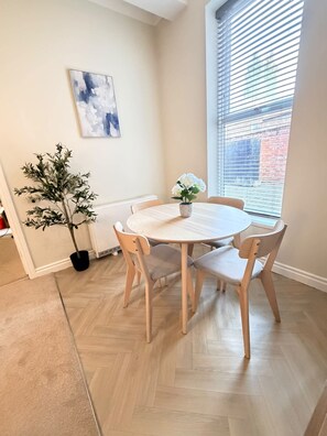 A dining area with a round table and four chairs, a potted plant, and a window with blinds. - Free On-site Parking - Central - WIFI - Grd Floor (Darlington)