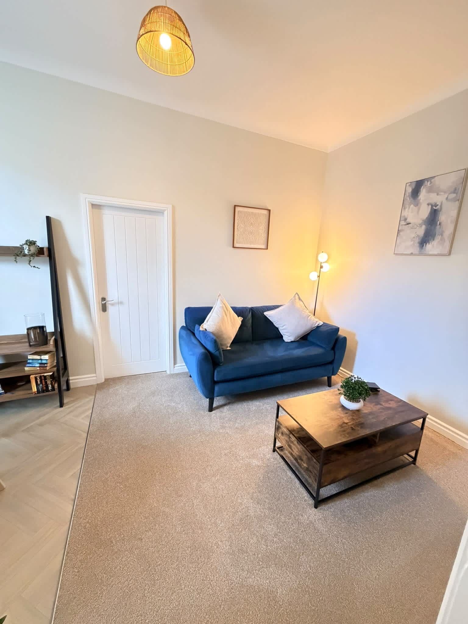 A living room with a blue sofa, a coffee table, a door, and a wall-mounted lamp.