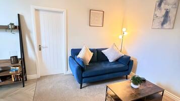 A living room with a blue sofa, a coffee table, a door, and a wall-mounted lamp.