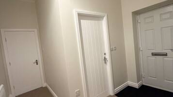 A hallway with two white doors, beige carpet, and a black carpeted area leading to another room.