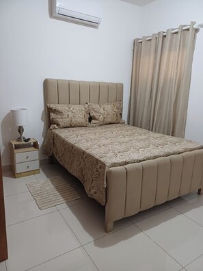 A bedroom with a bed, a bedside table, a lamp, and a curtain. - Sunrise: 3 Queen Bedrooms, Upstairs Lounge, Pool & Beach Nearby (Puerto Plata)