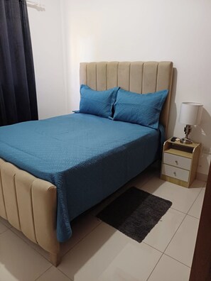 Ein Schlafzimmer mit einem Bett, einem Nachttisch, einer Lampe und einem dunklen Vorhang.